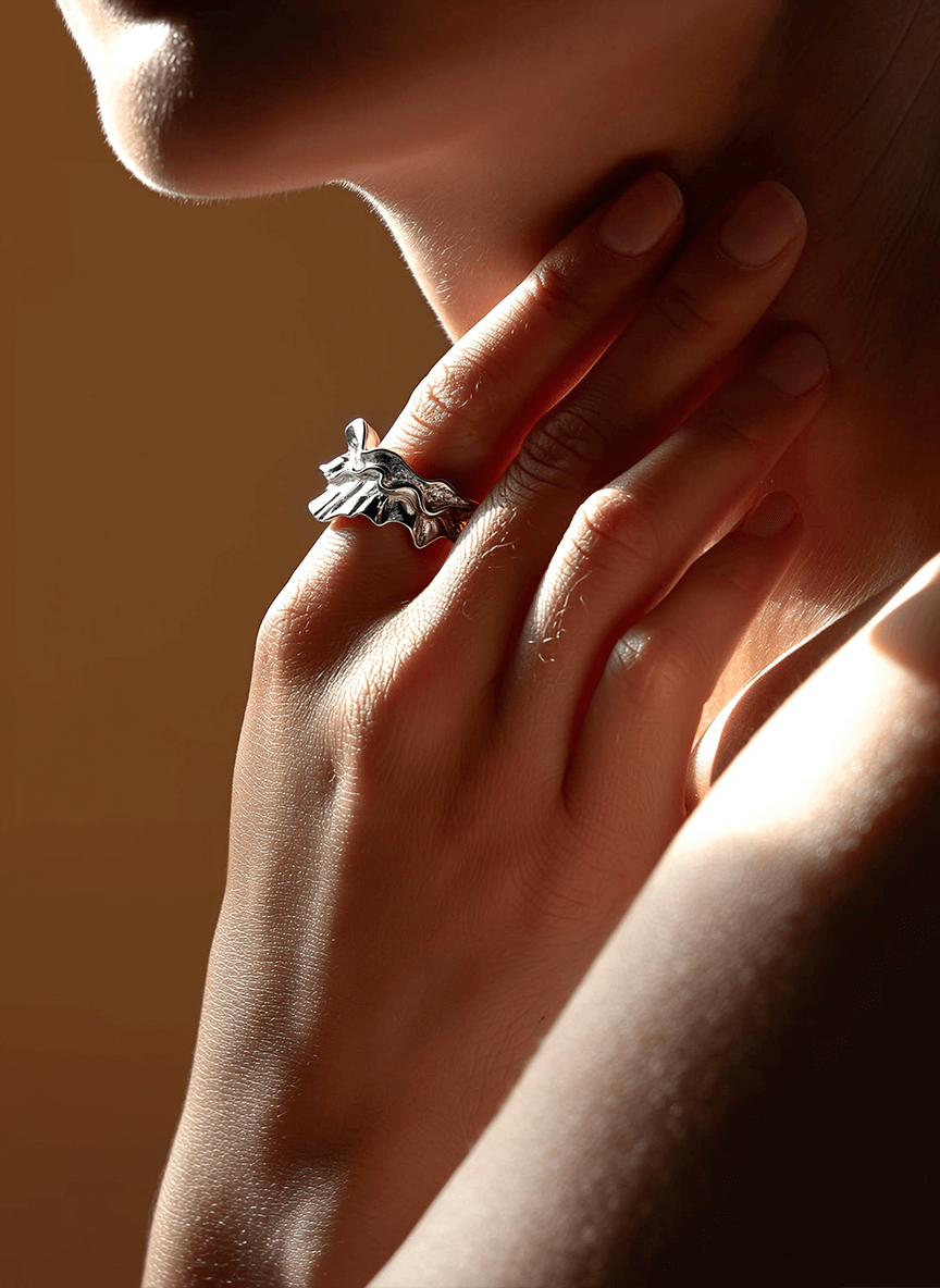 Close-up of a hand wearing a silver ring with a leaf design on a warm-toned background