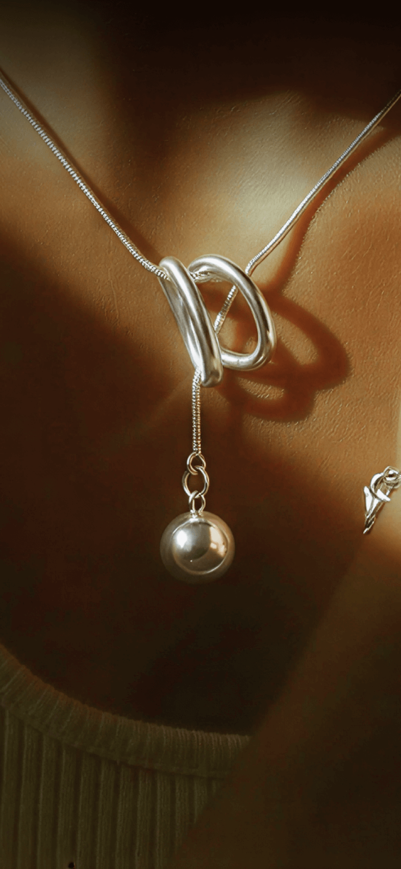 Silver necklace with a heart-shaped clasp and pearl pendant on a neutral background